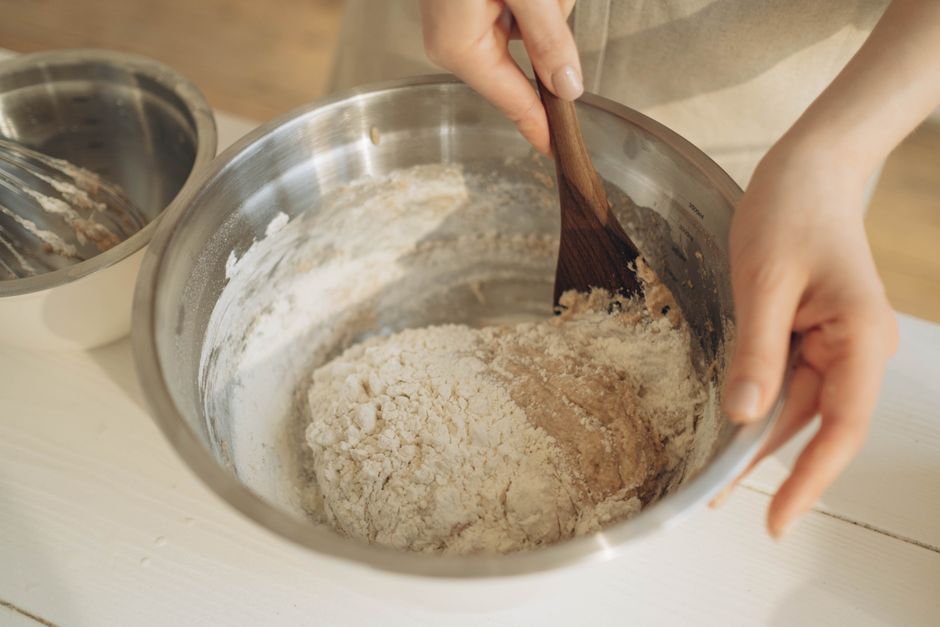 Ultimate Tender Banana Bread Recipe with Cake Flour 2 A baker gently folding dry cake flour into a wet banana mixture using a red rubber spatula in a glass mixing bowl.
