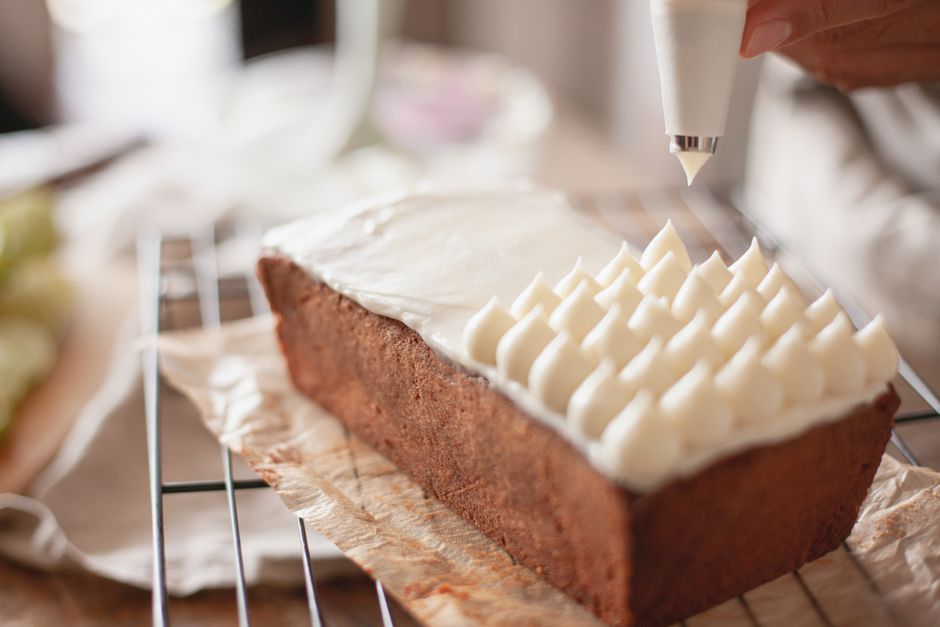 The Ultimate Guide to Frosting for Banana Bread Recipes 3 A baker using an offset spatula to spread smooth, white frosting over a cooled loaf of banana bread