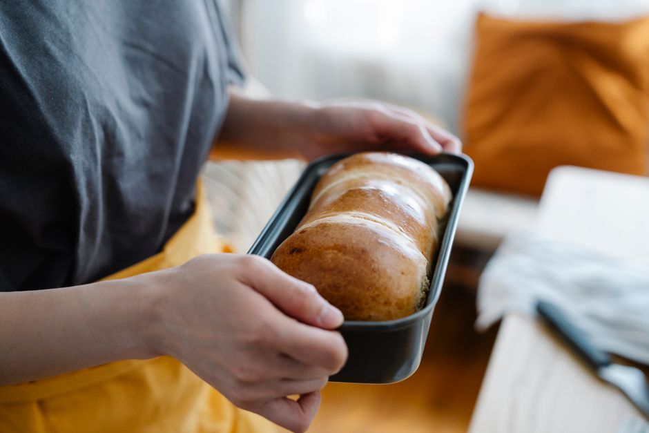 A close-up of a hand pouring a thick, glossy white glaze from a measuring cup onto a loaf of banana bread