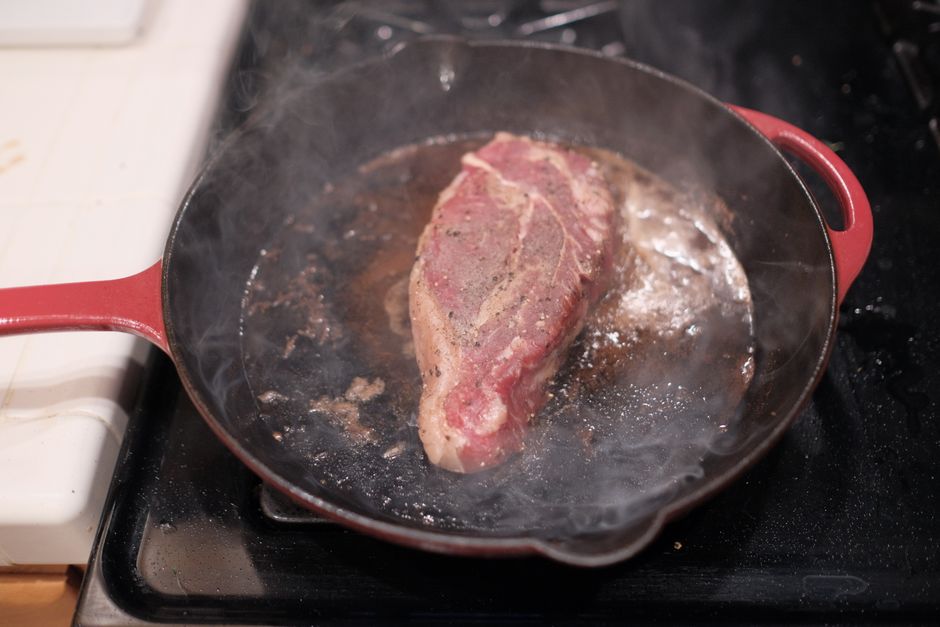 A close-up of a sizzling steak being seared in a cast-iron skillet with oil splashing slightly