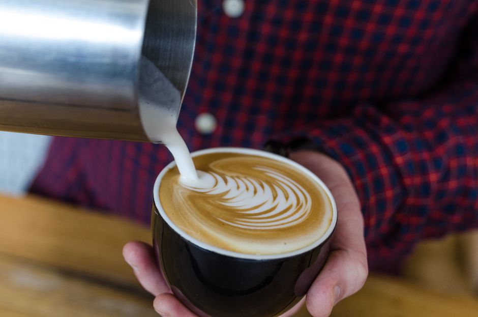 A close-up of frothed milk being poured into a cup of espresso, creating beautiful latte art topped with cinnamon