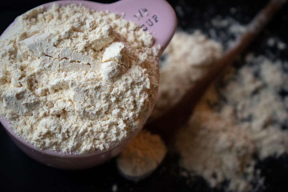A close-up of King Arthur unbleached all-purpose flour being measured into a metal cup next to ripe bananas