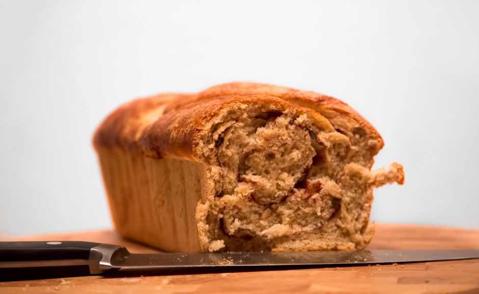 Ultimate Cinnamon Roll Banana Bread Recipe with Cream Cheese Glaze 1 A close-up shot of a sliced loaf of cinnamon roll banana bread, showcasing the intricate cinnamon swirl inside and the cream cheese glaze dripping down the sides.