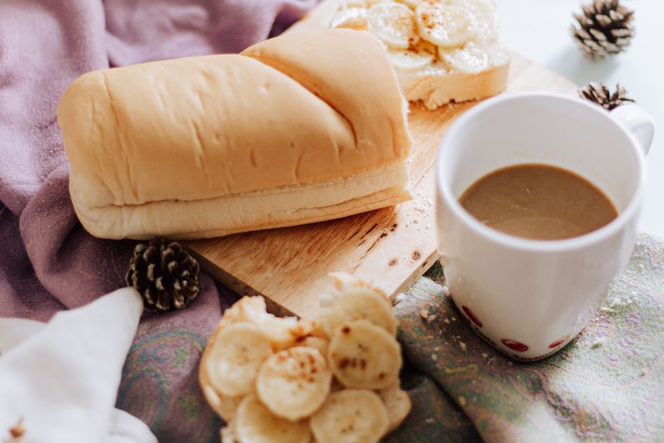 A cozy mug of banana bread latte sitting on a rustic wooden table next to a slice of fresh banana bread