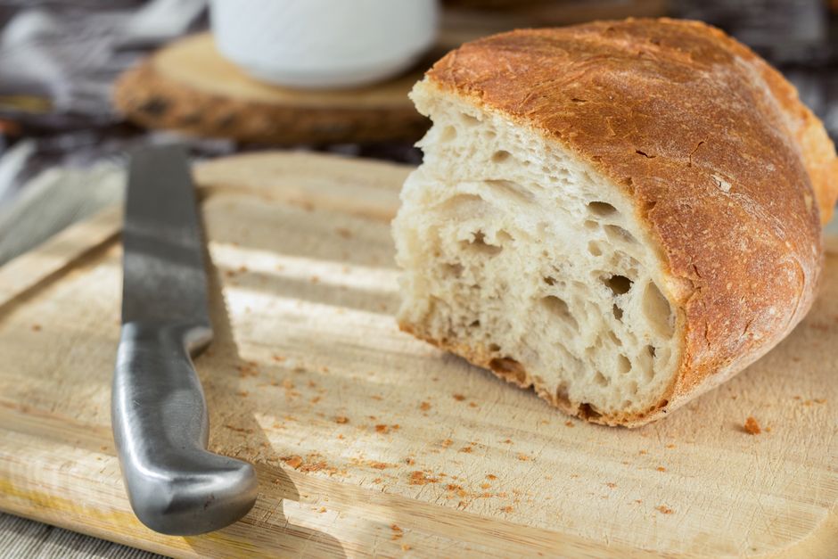 A freshly baked loaf of pineapple banana bread resting on a rustic wooden cutting board, with a slice cut to reveal the moist crumb and yellow pineapple bits.