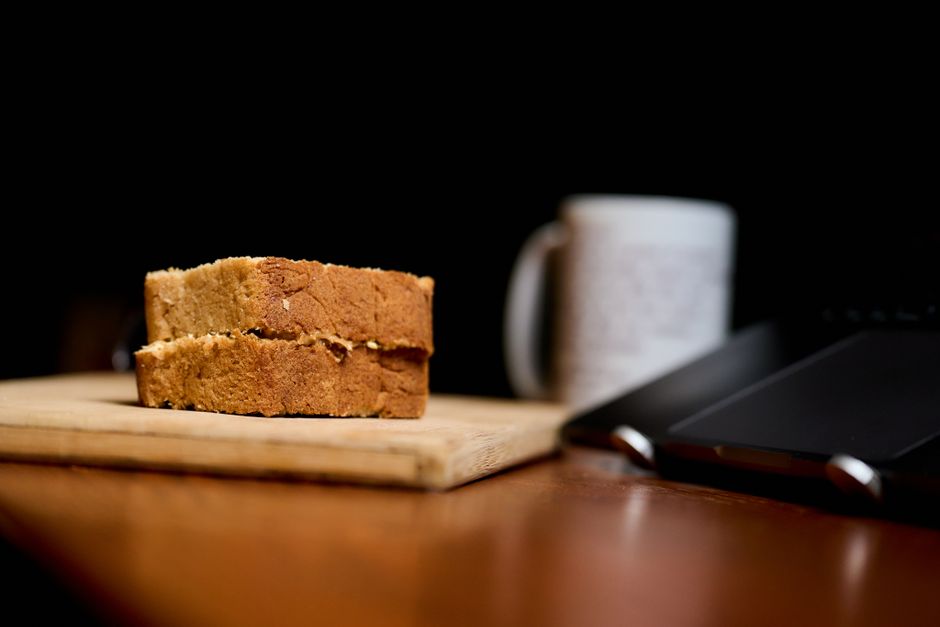 A freshly sliced loaf of golden brown banana bread sweetened with Splenda, sitting on a wooden cutting board with a cup of coffee nearby