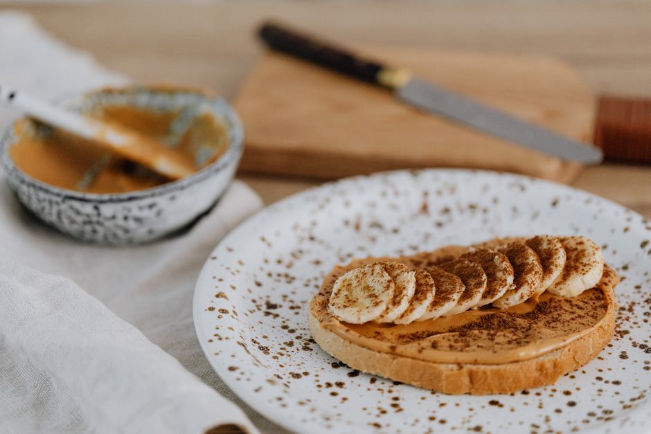 A slice of chocolate banana bread toasted and spread with peanut butter, next to a steaming mug of coffee