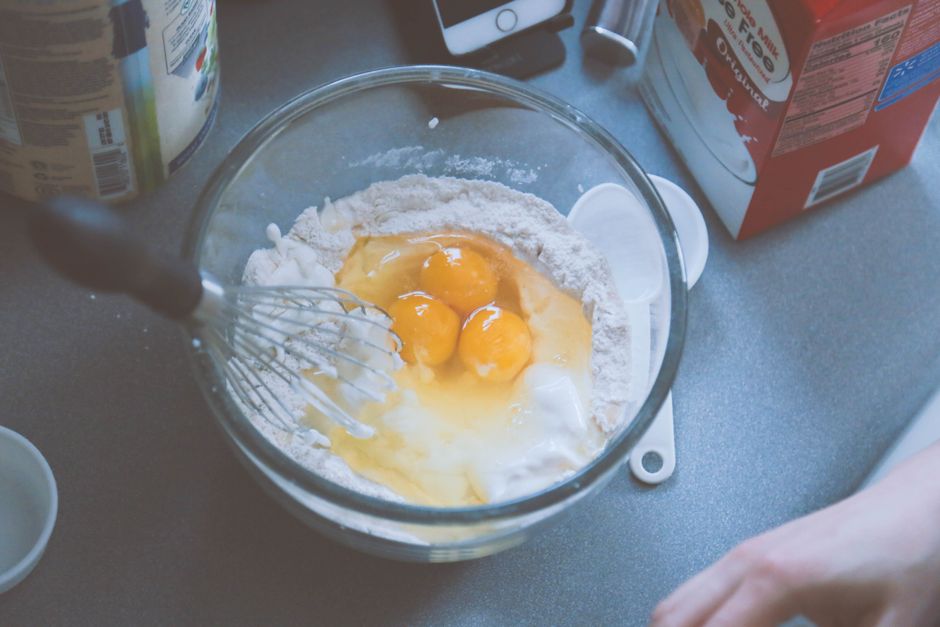A step-by-step shot showing mashed bananas being mixed with maple syrup and eggs in a glass bowl